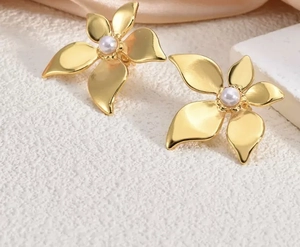 Detail of gold petal earrings with white pearls on a minimalist stone background