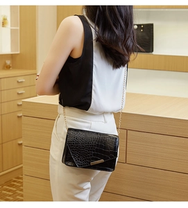 Detail of black faux crocodile skin shoulder bag with gold chain strap worn by a model
