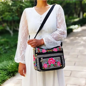 Detailed peony floral embroidery on a black ethnic crossbody bag worn by a model