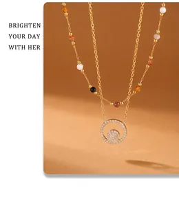 Détail d'un collier doré double épaisseur avec perles colorées et pendentif zircon