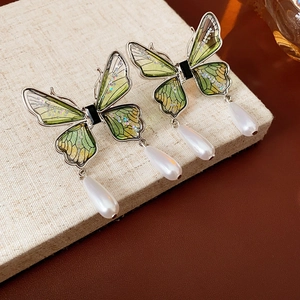 Detail of green sequin butterfly earrings with waterdrop pearls on beige fabric base