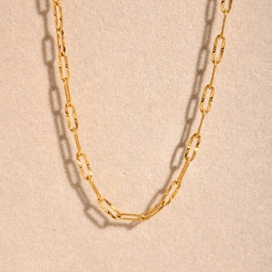 Macro shot of gold paperclip chain link showing textured faceted finish and metallic glow