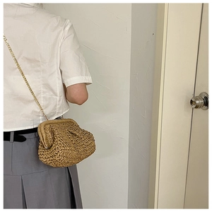 Detailed close-up of a light brown woven straw clutch with a gold chain strap on a model