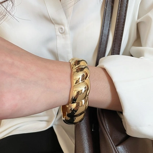 Gros plan d'un bracelet manchette torsadé doré porté par un mannequin en chemise blanche