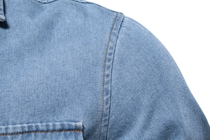 Close-up of shoulder stitching on a light blue denim shirt with orange contrast thread