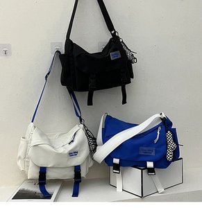 Three oversized nylon messenger bags in black, white, and blue with checkered charms