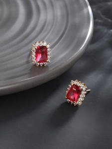 Detail view of gold earrings with rectangular red gems and white zircon halo on a tray
