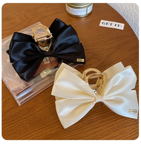 Detail view of premium silk bow hair claws in black and cream with gold metal clips