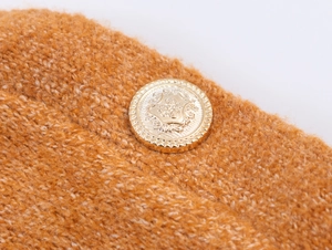 Dettaglio macro del tessuto a maglia caramello con bottone araldico in metallo dorato