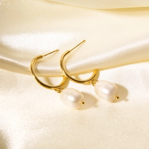 Macro view of French style gold hoop earrings with natural pearls on beige silk fabric