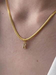 Primo piano della collana a catena serpente dorata con ciondolo lettera R in cristallo