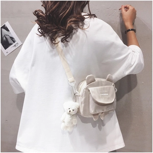 Model wearing a small cream canvas crossbody bag with a cute plush bear charm detail