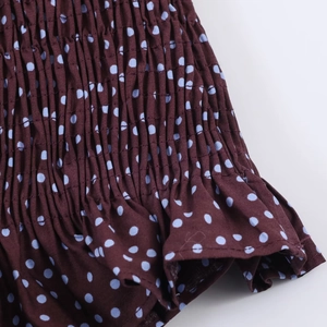 Detail of polka dot print on tan fabric with elastic smocked texture and ruffle trim