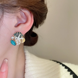 Close-up of ocean-themed earrings featuring blue shells, starfish, and conch on a model
