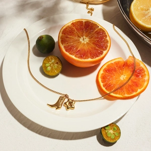 Detail of 18K gold star and boot pendants on a necklace over fresh fruit platter