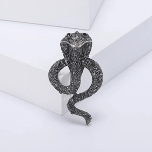 Vintage silver cobra brooch with dark rhinestones on a minimalist white background