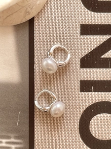 Macro detail of 925 sterling silver hoop earrings with white freshwater pearls on fabric