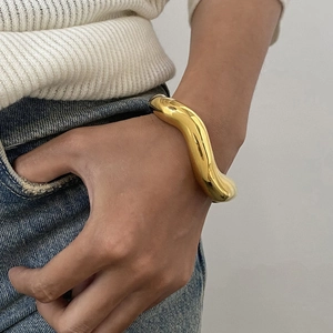 Minimalist thick wave open cuff bracelet in polished gold finish worn on wrist