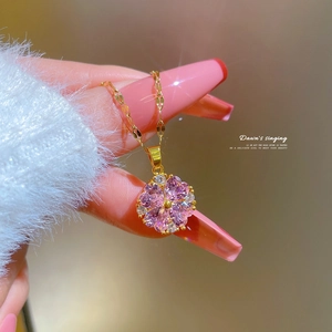Close-up of golden clover pendant with pink gemstones and pavé crystals on a dainty chain