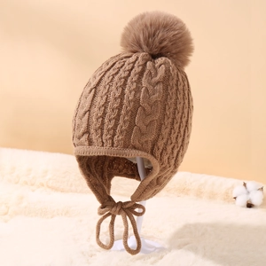 Detailed knit texture of a brown cable-knit baby winter hat with a fluffy faux fur pompom