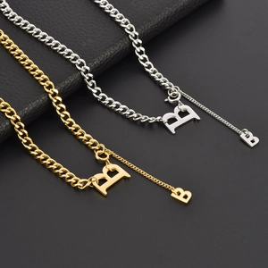 Colliers gourmettes or et argent avec pendentifs lettre B sur fond sombre texturé