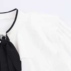 Detail of white shirt neckline featuring a black bow tie and layered ruffle trim accents