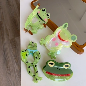 Details von vier grünen Frosch-Haarklammern aus Acetat auf einer weißen Fläche