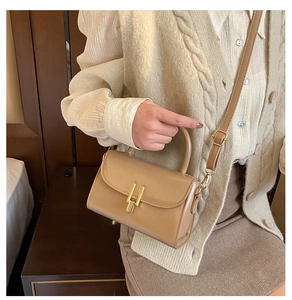 Detail of khaki leather handbag with gold twist lock worn by model in soft natural light