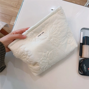 Detail of white quilted cosmetic bag with floral embroidery and Simple Wish fabric label