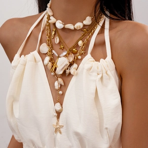 Detail of layered gold necklace with seashell, starfish charms and faux pearls