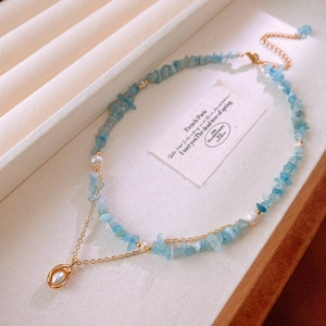 Close-up of aquamarine stone necklace with freshwater pearls and gold chain on beige tray