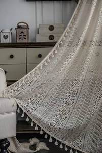 Detail of bohemian crochet lace curtain with geometric hollow patterns and handmade tassels