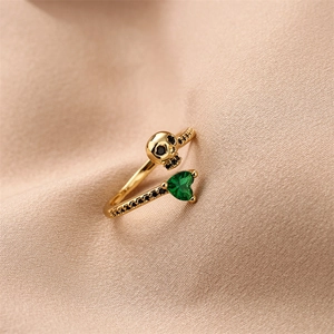 Close-up of gold skull ring with heart-shaped green stone and black crystals