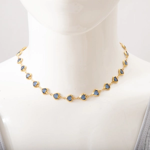 Close-up of gold titanium necklace with blue heart-shaped gems on white mannequin