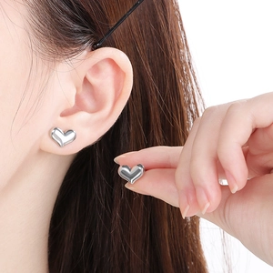 Macro detail of polished silver heart-shaped stud earrings worn by a model