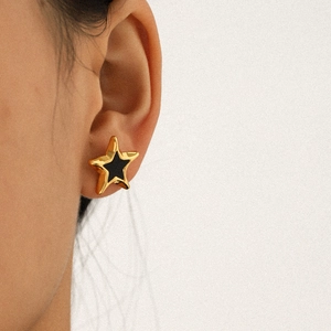 Close-up of model wearing a golden star earring with black inlay detail on white background