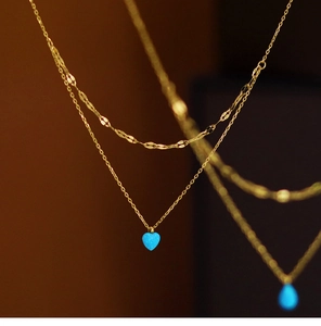 Close-up of tiered gold chains with blue heart and teardrop opal pendants on warm background