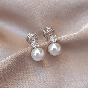 Elegant silver zircon pearl clip-on earrings displayed on champagne silk fabric
