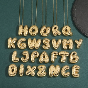 Golden bubble initial pendants with cubic zirconia inlay on a green textured surface
