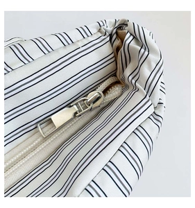 Détail de la fermeture éclair en métal argenté et du tissu rayé noir et blanc du sac