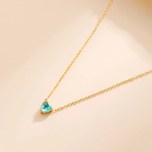 Macro detail of a 18k gold heart-shaped pendant necklace with light blue crystal