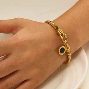 Detail of 18k gold plated cable bracelet with Roman numeral black enamel charm on model