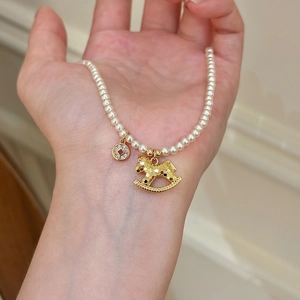 Détail d'un bracelet en perles avec un charm de cheval doré et un pendentif de pièce serti