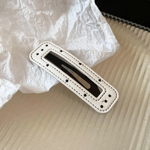 Close-up of a white leather BB hair clip with black polka dots and fine stitching detail