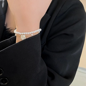 Detail of double-layer gold pearl bracelet with white camellia flower pendant on wrist