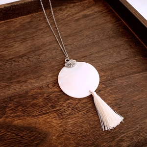 Detailed shot of silver necklace with white shell pendant and beige cotton tassel on wood