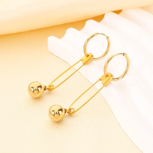 Close-up of golden geometric safety pin earrings with bead charms on a textured surface