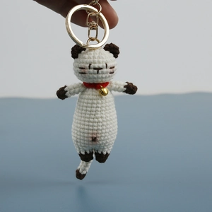 Handmade crochet Siamese cat keychain with red collar and golden bell on blue background