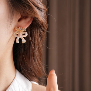 Close-up of golden bow earrings with white enamel and pear-cut cubic zirconia on a model