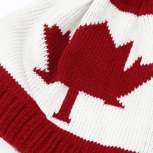 Detailed close-up of a white knit beanie featuring a red maple leaf and ribbed edge
